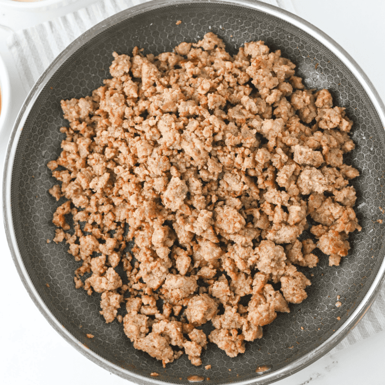 Pork sausage browning in a large skillet, broken into small pea-sized crumbles