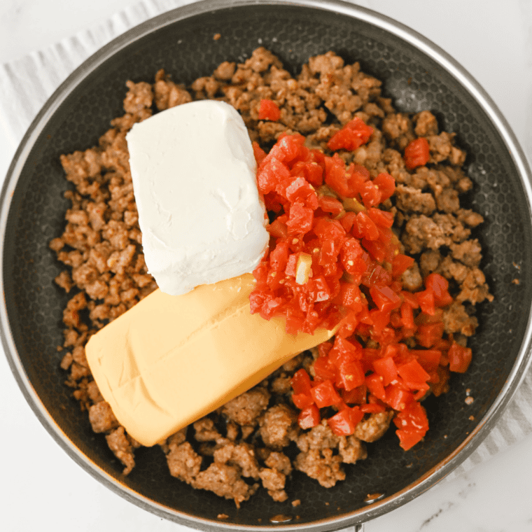 Cubed Velveeta, cream cheese and drained Rotel added to browned sausage in a skillet