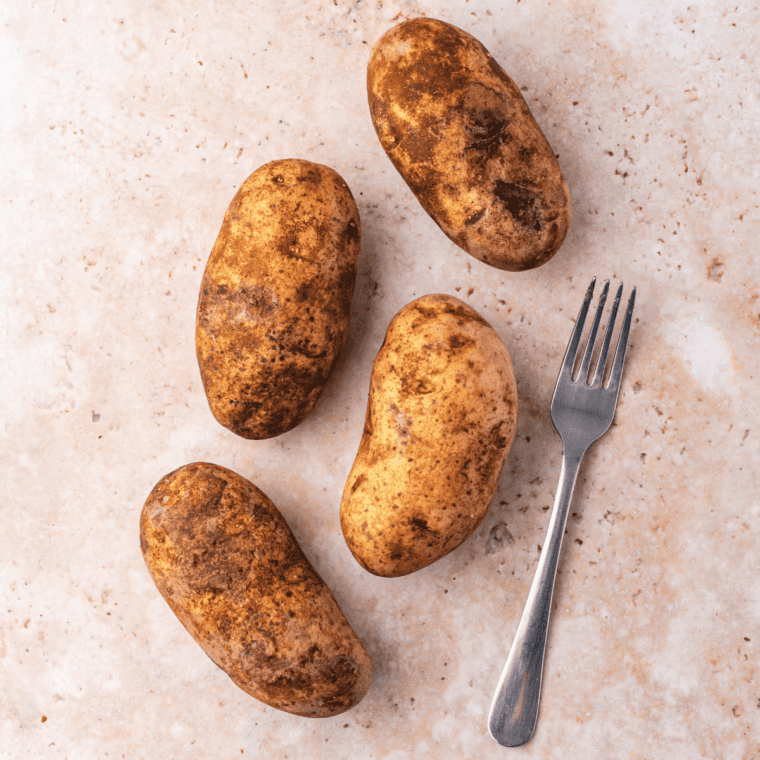 Fork piercing holes across the surface of a raw russet potato