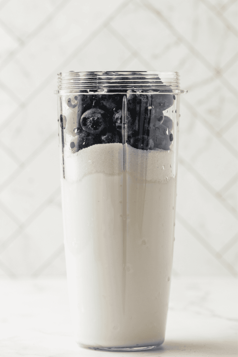 Pouring blueberry yogurt base into a Ninja Creami pint below the max fill line