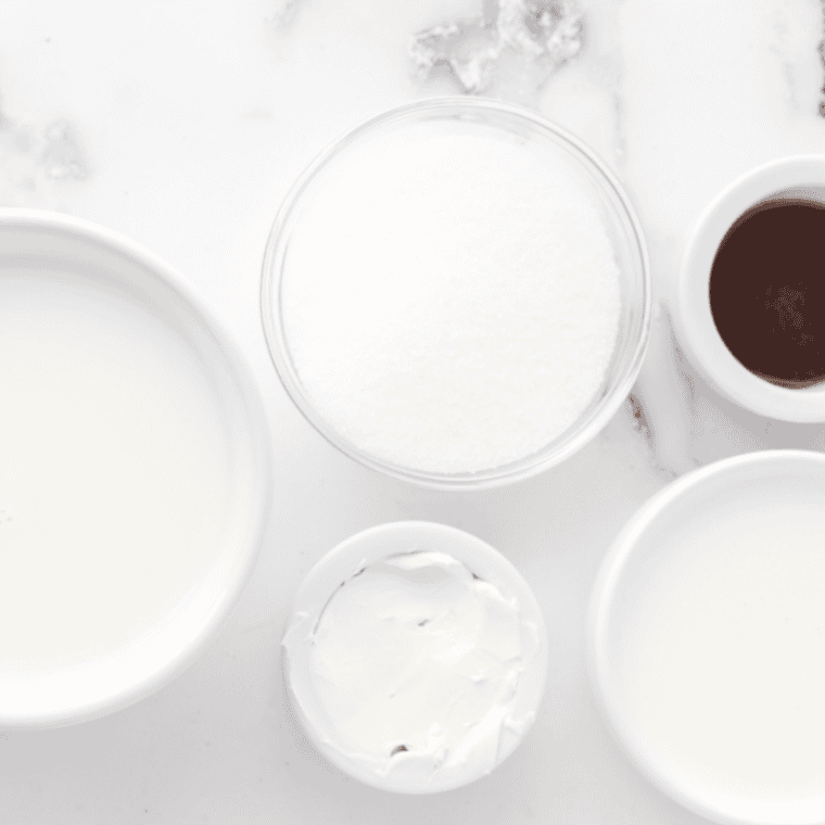 Greek yogurt, cream cheese, milk, sugar, lemon, and vanilla in bowls on a counter
