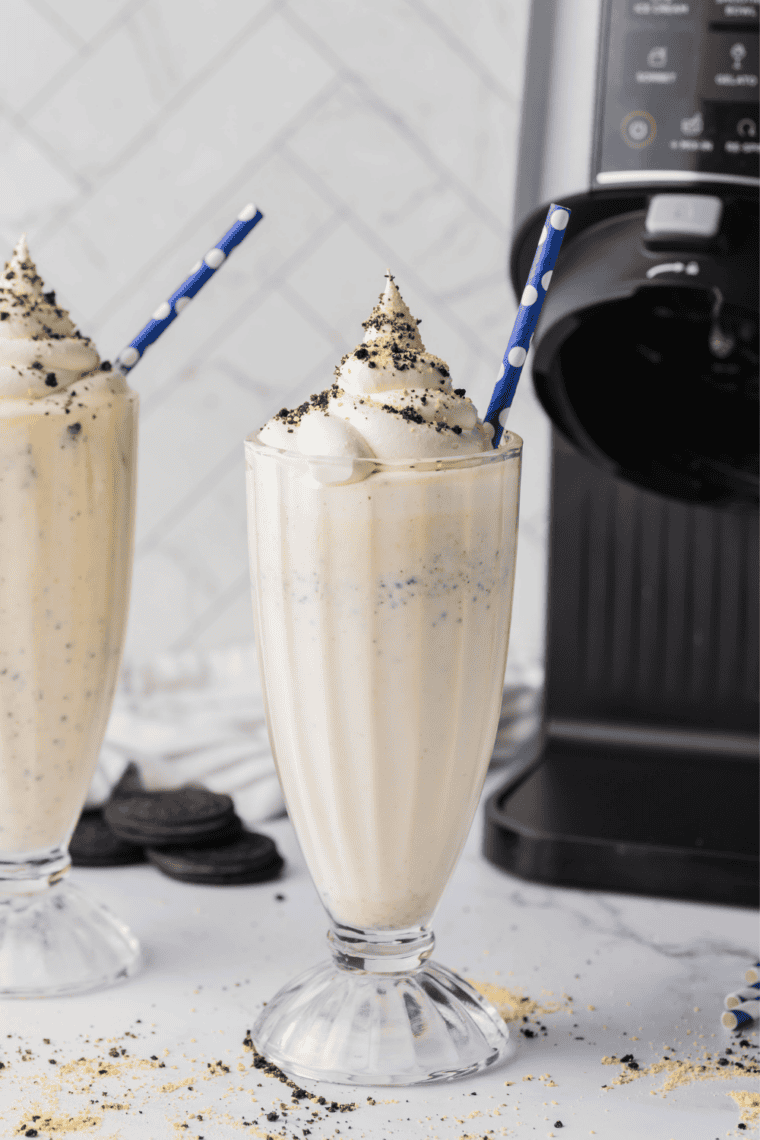 Ninja Creami Copycat Sonic Oreo Cheesecake Milkshake in a tall glass topped with whipped cream, crushed Oreos, and graham cracker crumbs