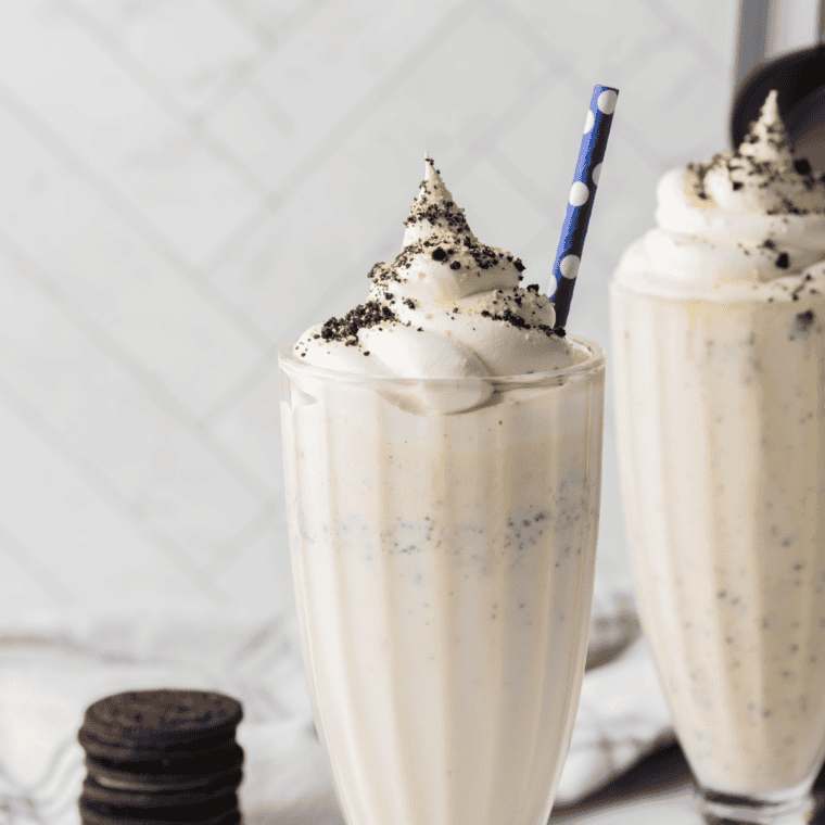 Ninja Creami Copycat Sonic Oreo Cheesecake Milkshake in a tall glass topped with whipped cream, crushed Oreos, and graham cracker crumbs