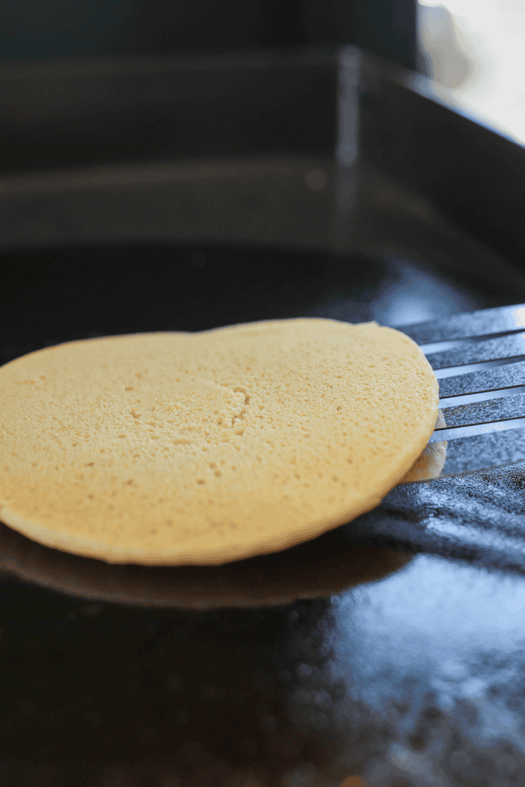 Stack of four golden buttermilk hotcakes on a white plate with a pat of butter