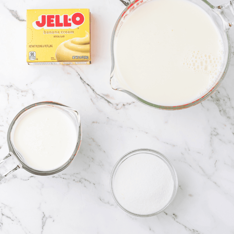 Ingredients for a Ninja Creami Steak 'n Shake banana shake laid out on a counter, including whole milk, heavy cream, sugar, a ripe banana, and vanilla extract
