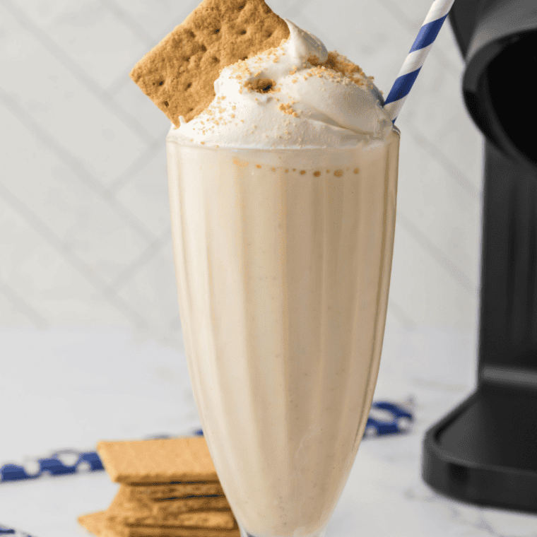 Finished Ninja Creami banana shake poured into a tall glass with whipped cream and a cherry