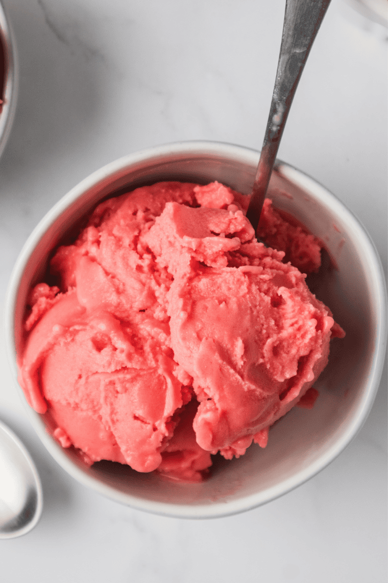 Ninja Creami strawberry Greek yogurt ice cream swirled in a pint container beside fresh strawberries