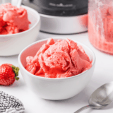 Scoop of Ninja Creami strawberry Greek yogurt ice cream in a white bowl topped with fresh strawberries