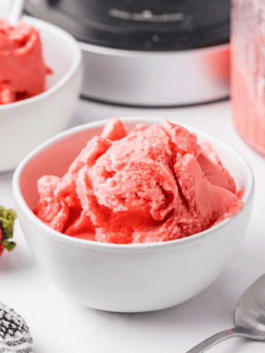 Scoop of Ninja Creami strawberry Greek yogurt ice cream in a white bowl topped with fresh strawberries