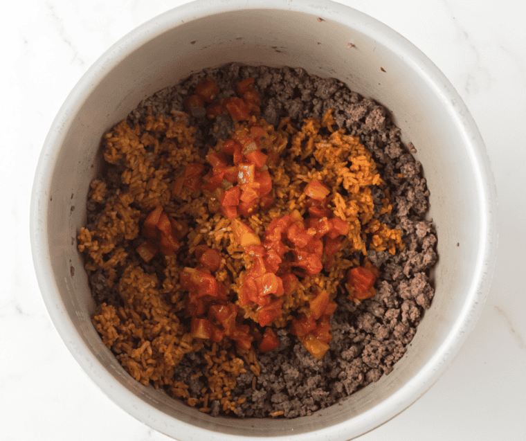 Ground beef browning in a skillet, broken into crumbles with a wooden spoon