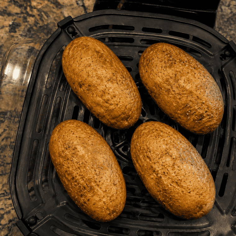 Four seasoned potatoes spaced apart on the crisper plate in a Ninja Crispi glass container