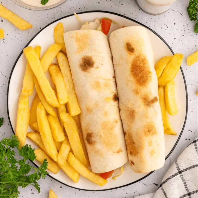 Four crispy rotisserie chicken snack wraps stacked on a white plate with a bowl of ranch