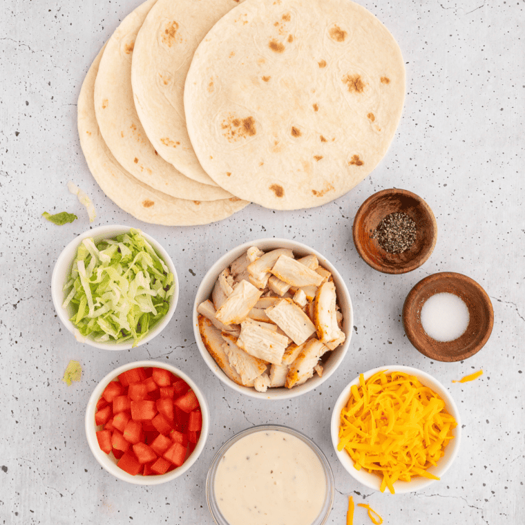 Ingredients for rotisserie chicken snack wraps: shredded chicken, flour tortillas, cheddar, ranch, lettuce, and diced tomatoes