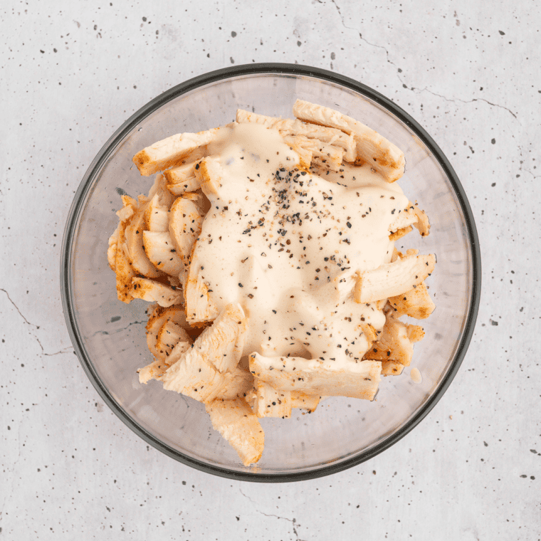 Shredded chicken and ranch dressing stirred together in a glass mixing bowl