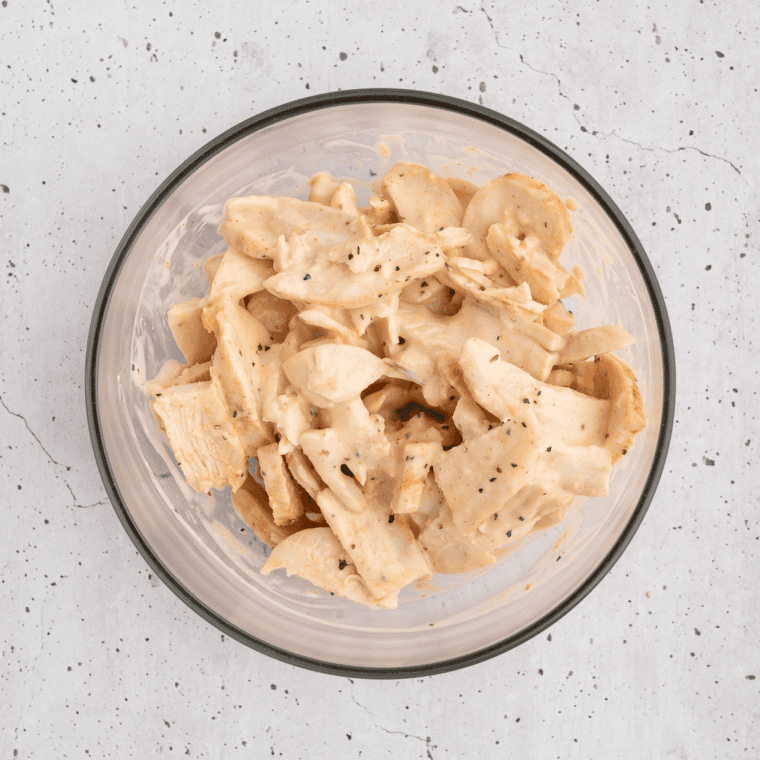 Shredded rotisserie chicken mixed with ranch dressing in a glass bowl
