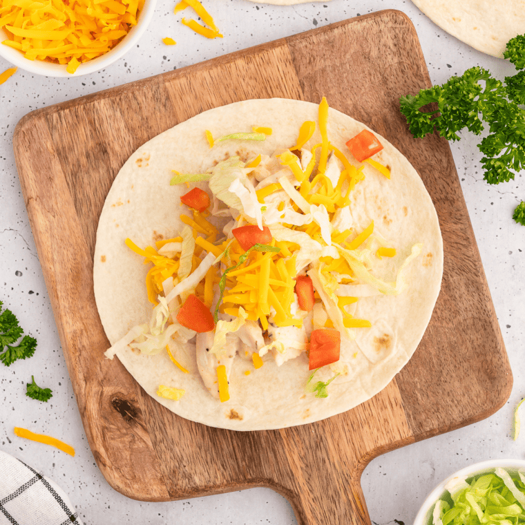 Hands folding in the sides of a tortilla and rolling it into a tight snack wrap
