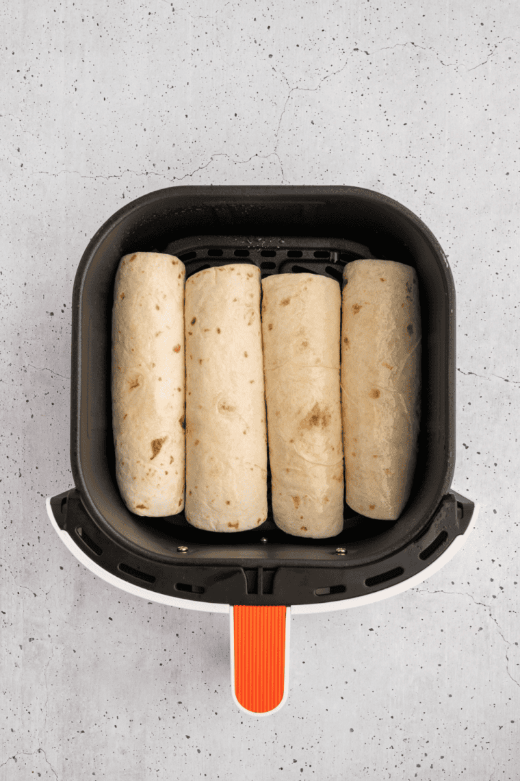 Four rolled wraps placed seam side down in an air fryer basket with space between them
