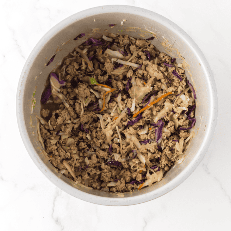 Slow cooker lid on with cabbage and ground chicken cooking down for chicken egg roll in a bowl