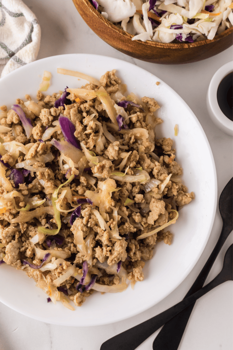 White bowl of slow cooker chicken egg roll in a bowl with shredded cabbage, ground chicken, and toasted sesame seeds