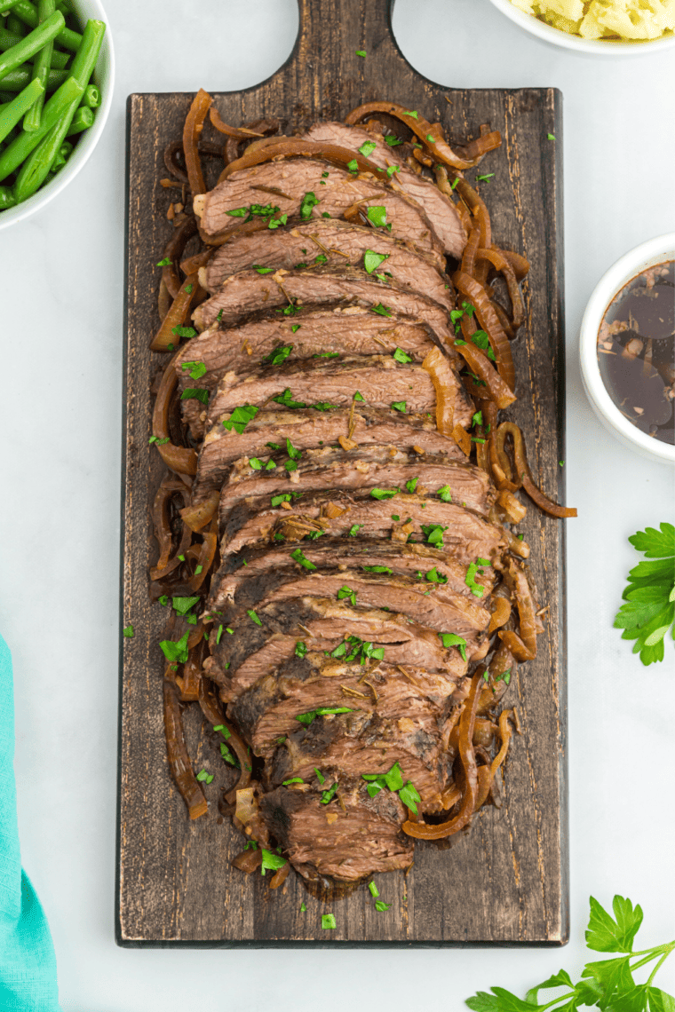 Sliced tri tip roast fanned out on a wooden cutting board with visible pink centers 