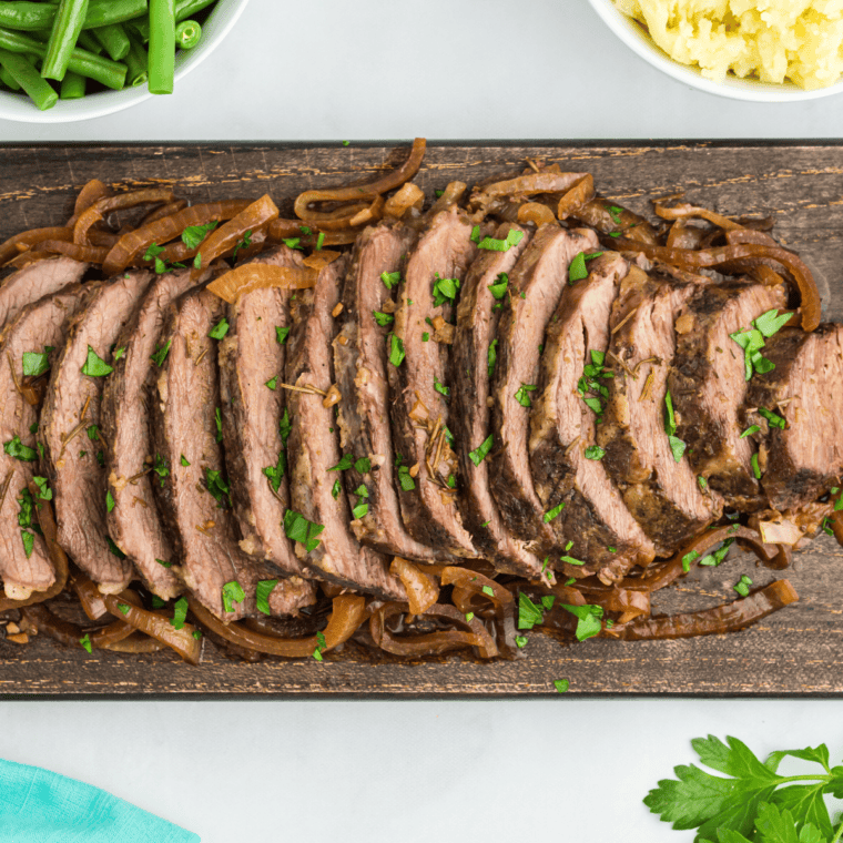 Tri tip roast sliced thin against the grain on a cutting board with juices pooling