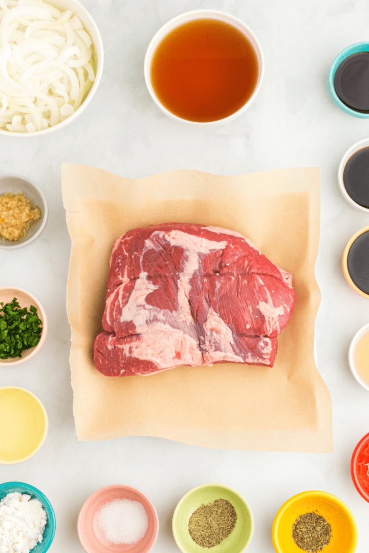 Slow cooker tri tip ingredients including a raw tri tip roast, seasonings, broth, and fresh rosemary