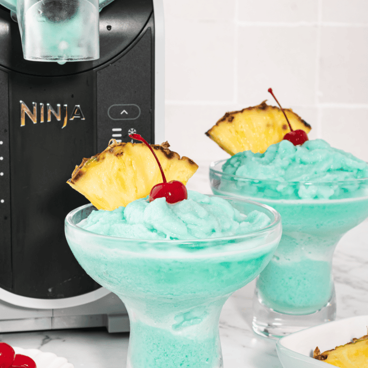 Two Blue Hawaiian slush drinks in glasses next to the Ninja Slushi machine on a kitchen counter