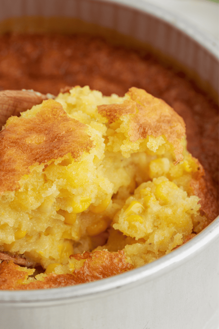 Scoop of creamy 12 Bones-style corn pudding on a plate next to BBQ ribs