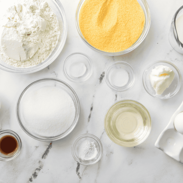 Ingredients for copycat 12 Bones Smokehouse corn pudding laid out on a table: fresh corn, eggs, heavy cream, butter, sugar, flour, and cheddar