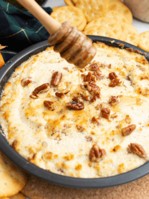 Baked goat cheese dip with honey, pecans, and fresh thyme in a white baking dish surrounded by toasted French bread slices