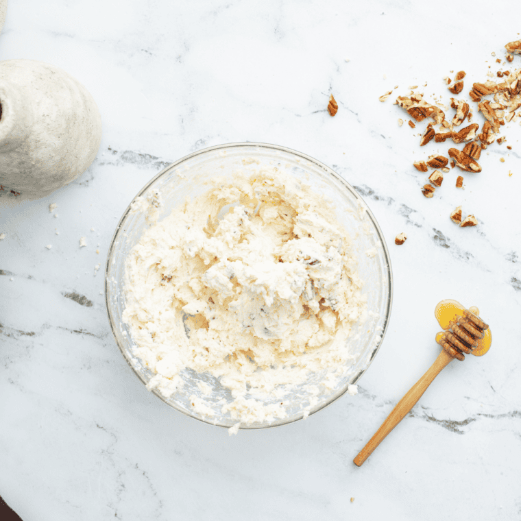 Creamy goat cheese dip mixture with pecans, honey, thyme, and lemon zest stirred together in a glass bowl