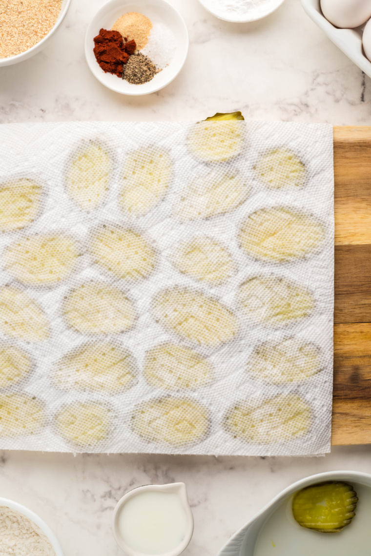 Hand pressing a paper towel on top of dill pickle chips to dry them before breading