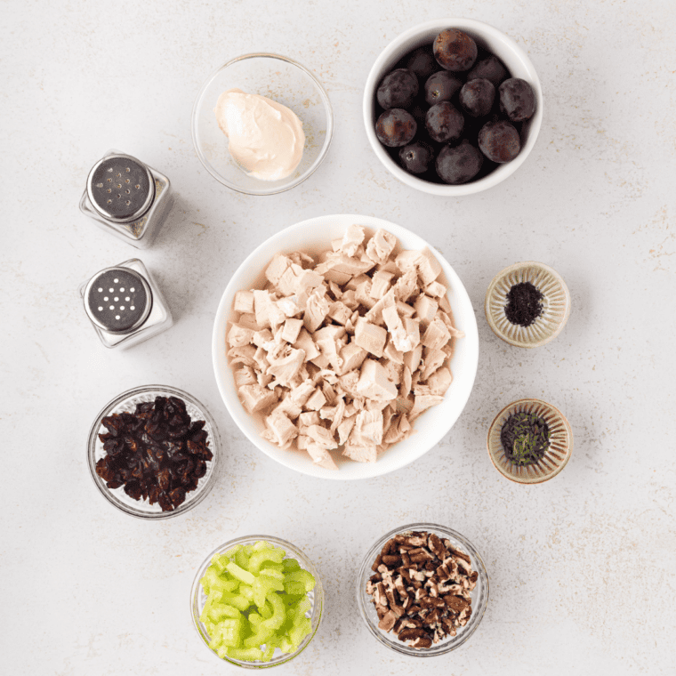 Ingredients for Amish hot chicken salad on a counter: cooked chicken, celery, onion, cheddar cheese, slivered almonds, Miracle Whip, lemon juice, and potato chips