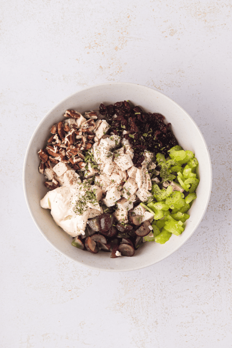 Mixing diced chicken, celery, onion, cheddar, almonds, and creamy dressing in a large bowl