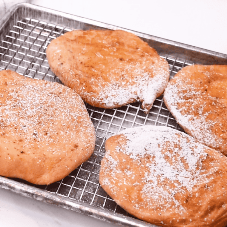 Four homemade Buc-ee's Beaver Tails drizzled with powdered sugar icing on a parchment-lined baking sheet