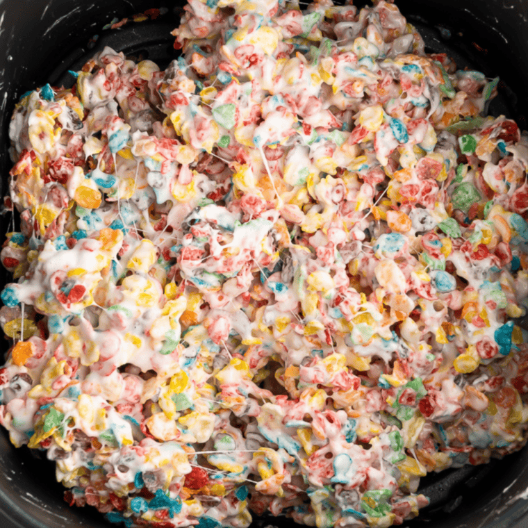 Fruity Pebbles and Rice Krispies being mixed into melted marshmallow in a large pot