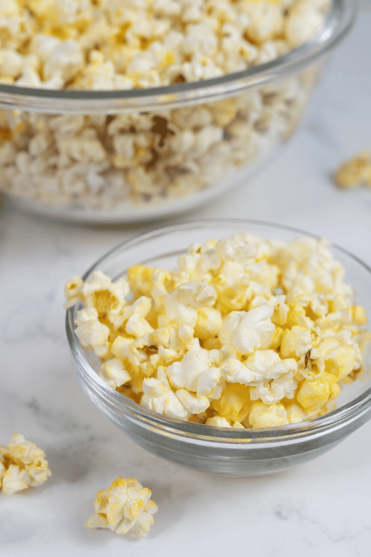 Kettle corn spread on a parchment-lined baking sheet with fine salt being sprinkled over the top