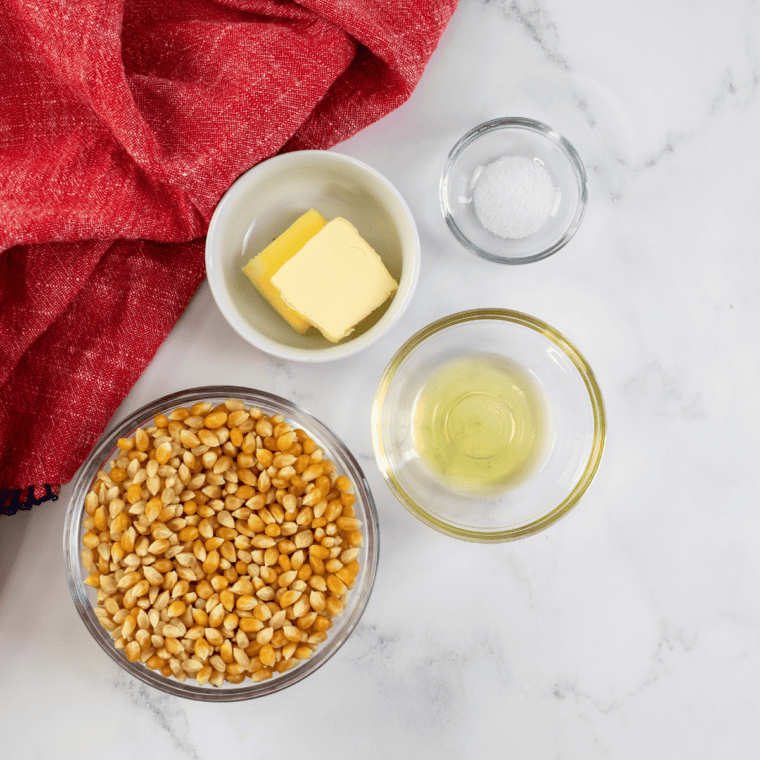 Popcorn kernels, vegetable oil, granulated sugar, and fine salt measured out in small bowls for homemade kettle corn