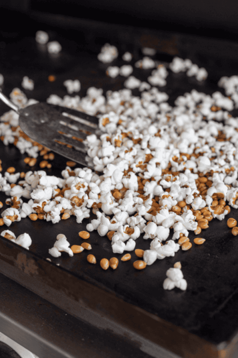 Popcorn kernels and granulated sugar being stirred into hot oil in a large pot