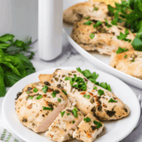 Copycat Carrabba's Tuscan Grilled Chicken sliced on a white plate with fresh parsley and lemon wedges