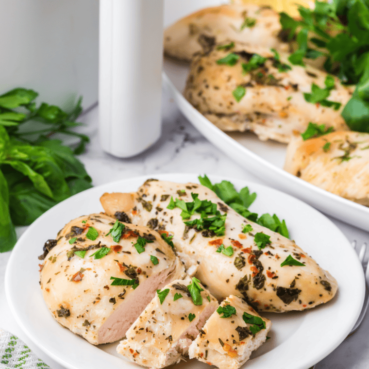 Copycat Carrabba's Tuscan Grilled Chicken sliced on a white plate with fresh parsley and lemon wedges