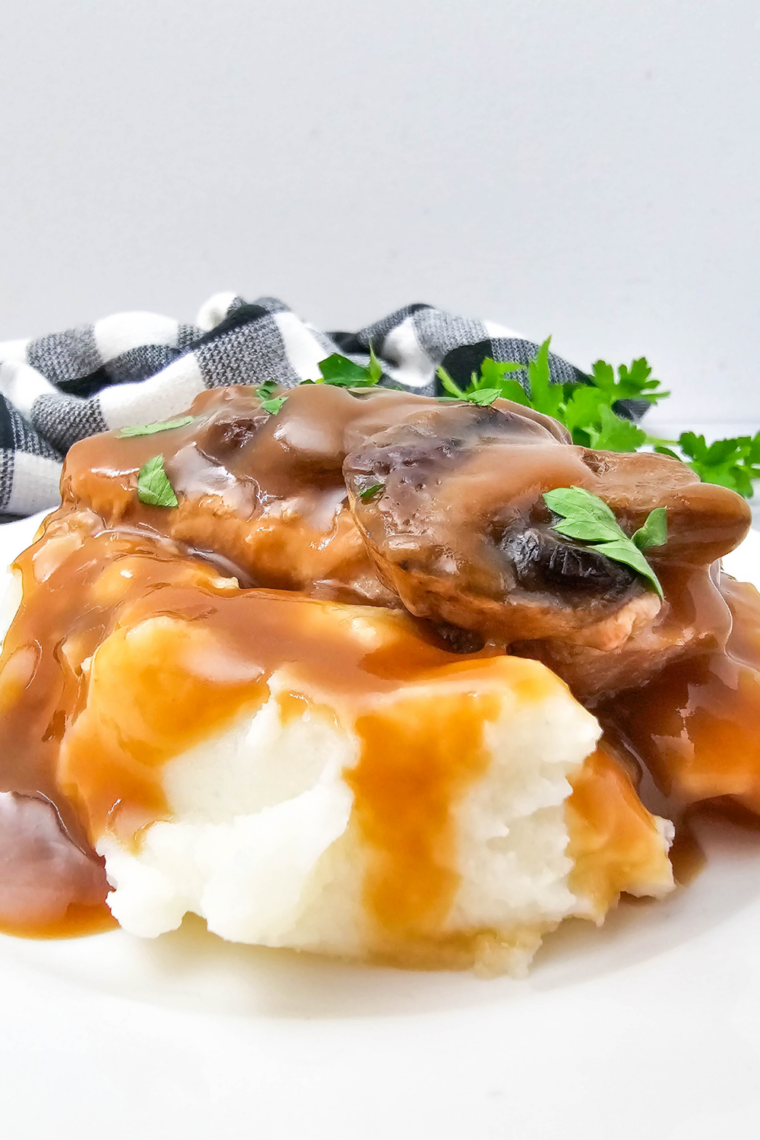 Homemade mashed potatoes on a white plate with savory brown gravy poured over the top