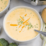 Copycat Denny's broccoli cheese soup in a white bowl topped with shredded cheddar