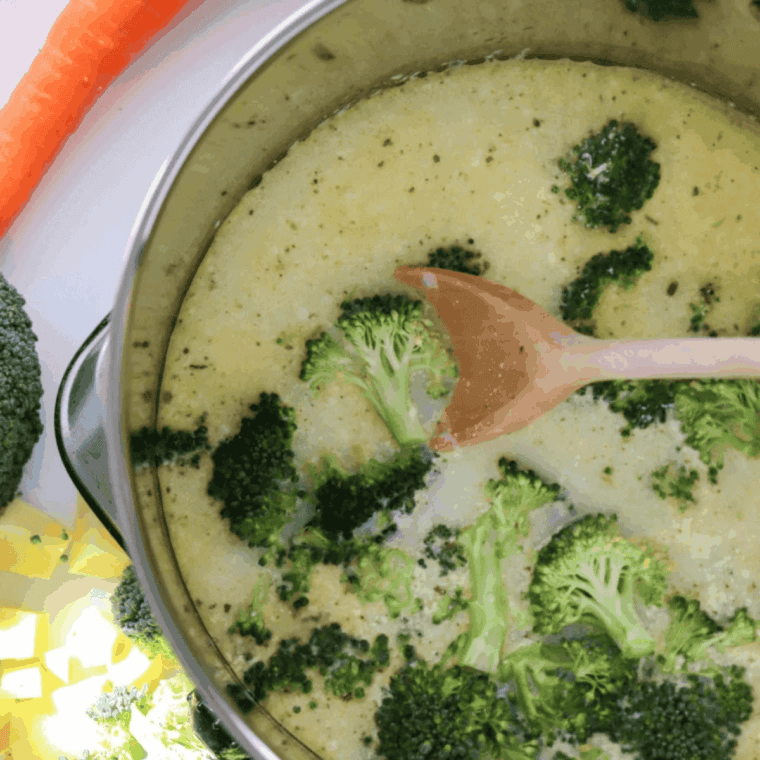 Adding chopped broccoli florets and shredded carrot to the soup pot