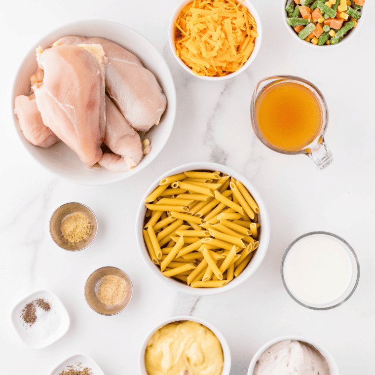 Ingredients for copycat Perkins chicken pot pie on a counter: cooked chicken, onion, celery, carrots, potato, butter, flour, chicken broth, cream, peas, and puff pastry