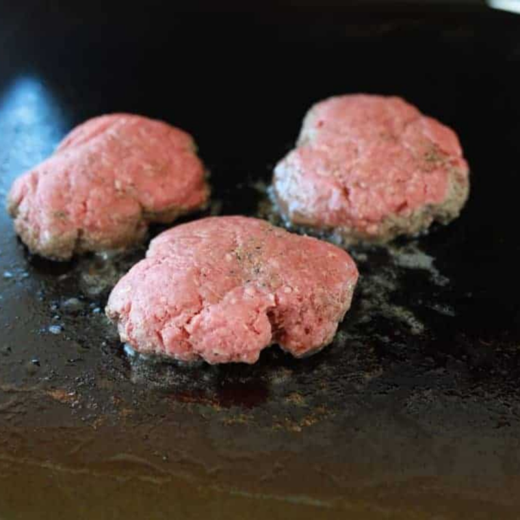 Beef ball smashed thin on a griddle with a burger press and parchment paper