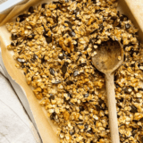 Cracker Barrel granola recipe with golden honey oat clusters, sliced almonds, and dried cranberries on a baking sheet
