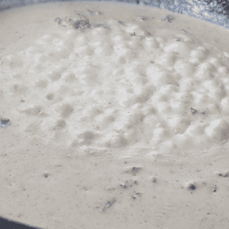 Thick, creamy country gravy simmering in a saucepan with coarse black pepper stirred in