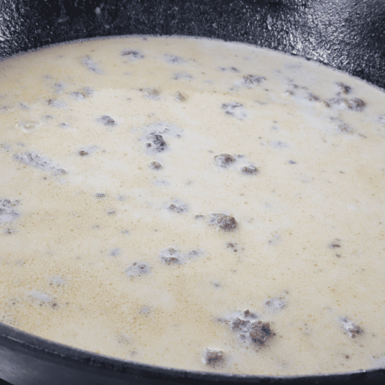 Slowly pouring whole milk into the roux while whisking to keep the gravy smooth