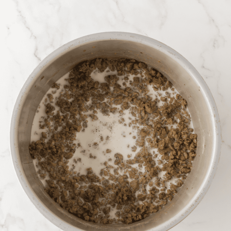 Cold whole milk being poured into the sausage roux and stirred into a creamy gravy